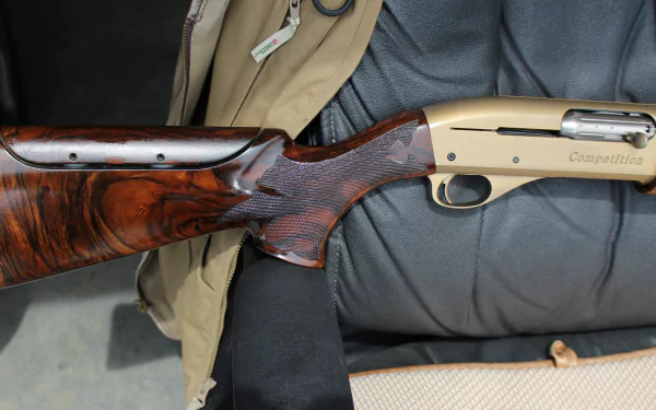 4K Ultra HD image of a man-made shotgun with a polished wooden stock and metallic body, resting on a leather chair and clothing.