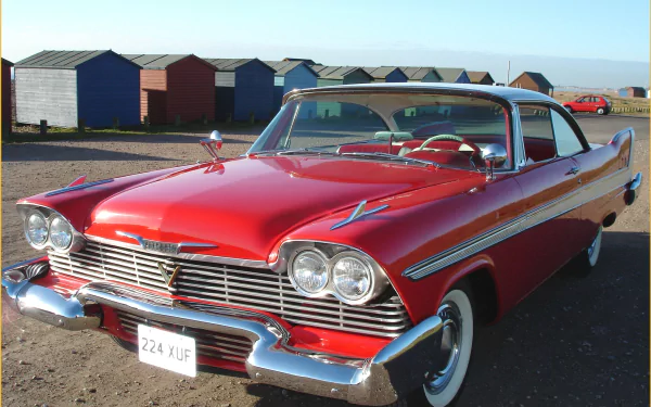 HD PC desktop wallpaper: red Plymouth Fury vehicle parked by seaside beach huts, showcasing classic chrome trim, dual headlamps and whitewall tires.