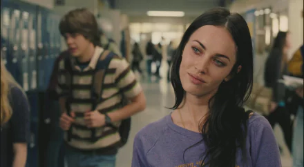 HD desktop wallpaper: dark-haired actress leaning in a high-school hallway, wearing a purple top and giving a sly, contemplative look in a cinematic horror-comedy film still.