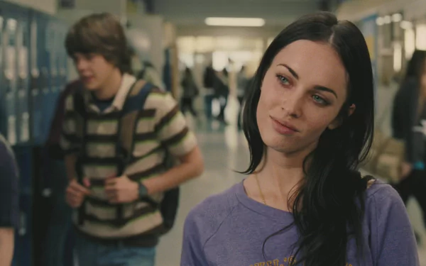 HD desktop wallpaper: dark-haired actress leaning in a high-school hallway, wearing a purple top and giving a sly, contemplative look in a cinematic horror-comedy film still.
