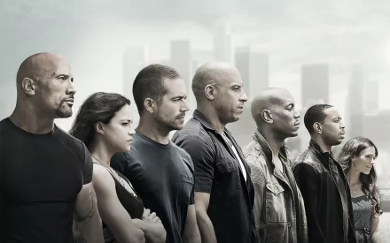 A dramatic HD wallpaper featuring the main cast of Furious 7: Dwayne Johnson, Vin Diesel, Paul Walker, Michelle Rodriguez, Tyrese Gibson, Ludacris, and Jordana Brewster, standing together.