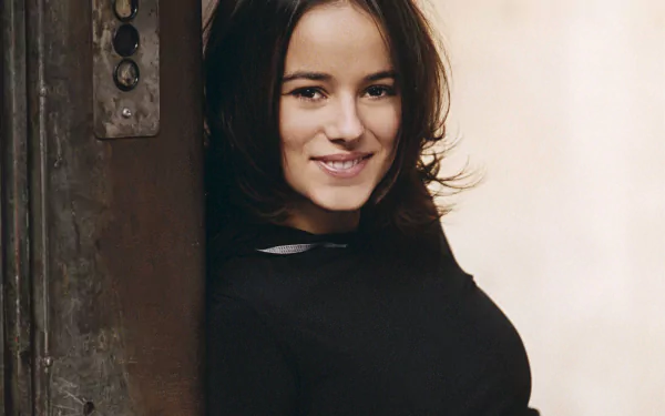 HD PC desktop wallpaper featuring Alizée smiling against a rustic background, capturing a warm and inviting music-themed portrait.