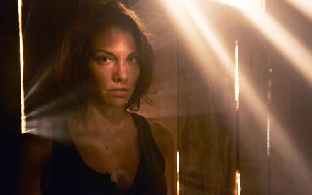A dramatic HD wallpaper featuring Lauren Cohan as her character from The Walking Dead, illuminated by rays of light filtering through wooden slats.