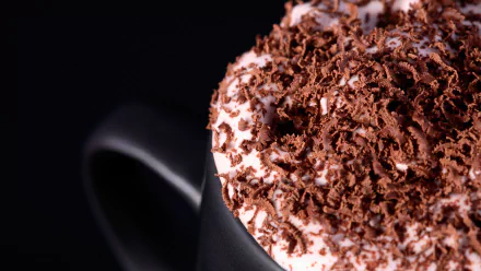 Close-up of a rich cappuccino topped with shavings of chocolate, set against a dark background. This HD desktop wallpaper highlights the indulgent details of the beverage.