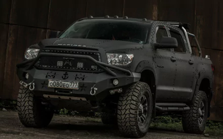 HD PC desktop wallpaper featuring a rugged black Toyota Tundra truck with off-road tires and custom front bumper in a dark industrial setting.
