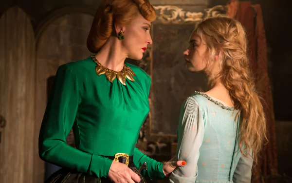 Two women in period costumes face off in a tense scene from Cinderella (2015); one in a vivid green gown with a gold necklace, the other in a pale blue dress.