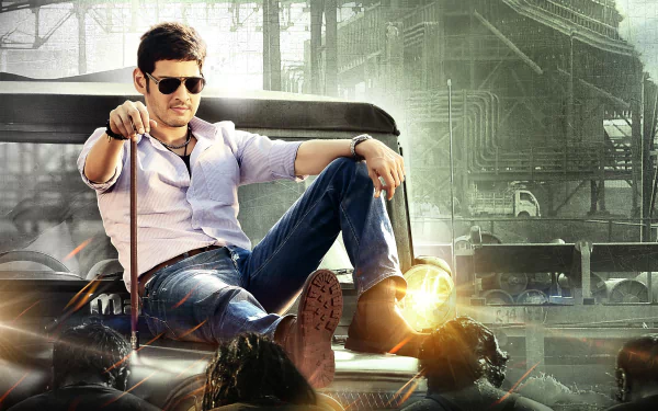 HD PC desktop wallpaper featuring celebrity Mahesh Babu casually seated against an urban industrial backdrop, showcasing a stylish and confident pose.