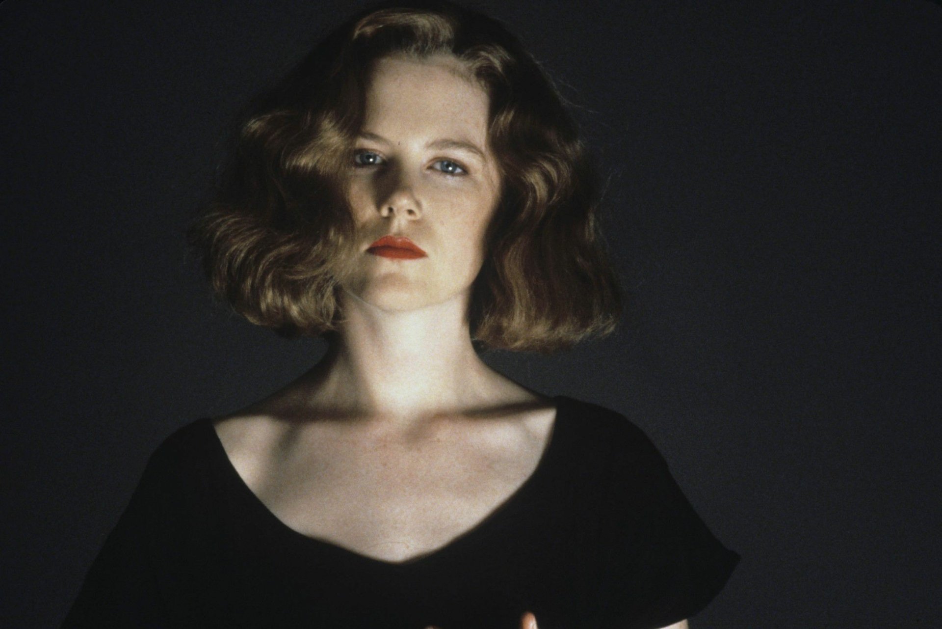 HD desktop wallpaper: moody studio portrait of a female celebrity with vintage wavy hair, red lips, and a black scoop-neck top against a dark background.