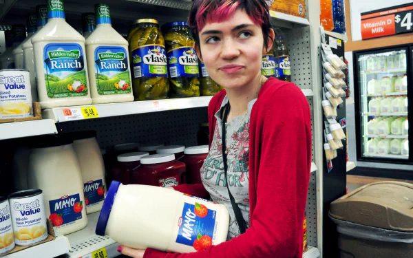 HD PC desktop wallpaper featuring musician Grimes holding a large jar of mayonnaise in a grocery store aisle, blending music and everyday life themes.