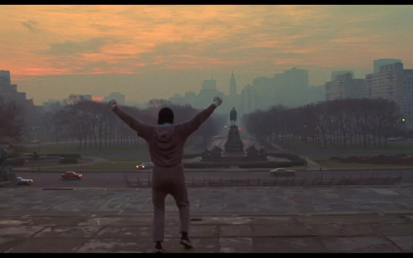 HD desktop wallpaper featuring a scene from the movie Rocky, showing a triumphant figure raising their arms in front of a cityscape at dawn.