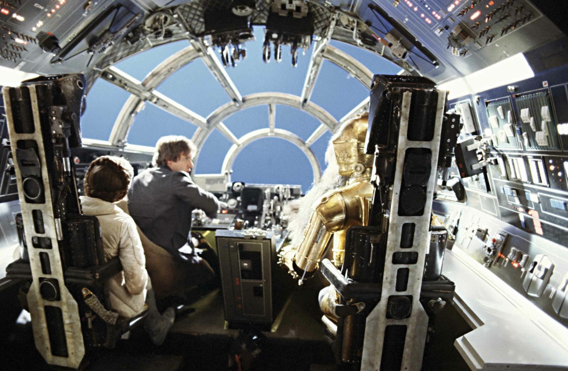 Star Wars movie HD PC desktop wallpaper: inside the Millennium Falcon cockpit with pilots and the golden droid C-3PO peering through the forward viewport at stars.