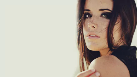 HD PC desktop wallpaper: close-up portrait of a woman with dark hair and light freckles looking over her shoulder against a pale, minimalist background.