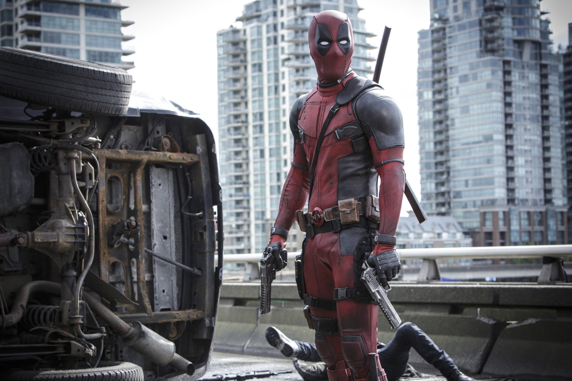Deadpool stands confidently in a cityscape, guns drawn, next to an overturned vehicle. This HD desktop wallpaper captures the bold essence of the iconic movie character.