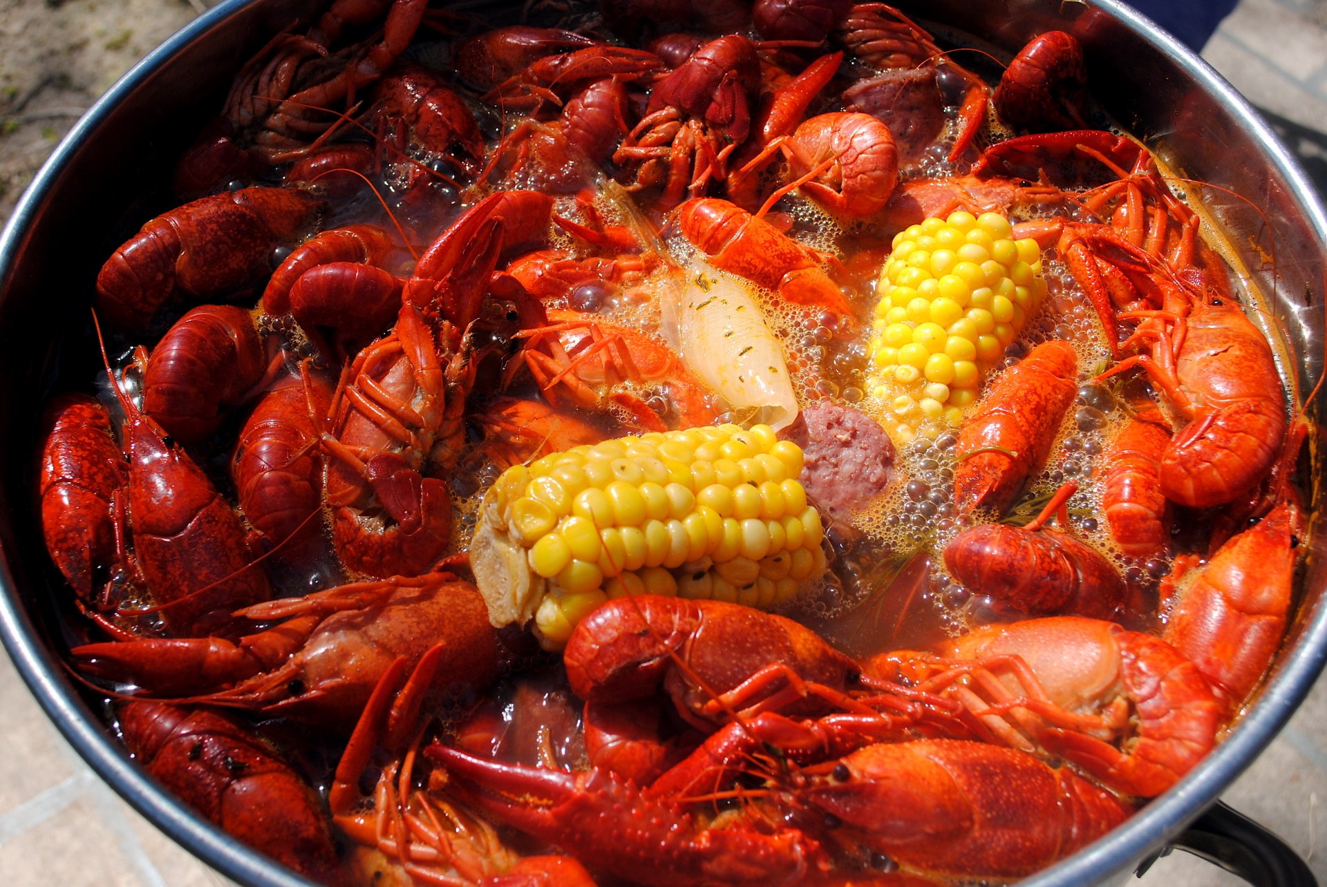 HD PC desktop wallpaper of a steaming crawfish boil: bright red crawfish with corn and sausage in a seasoned pot, vivid food close-up background.