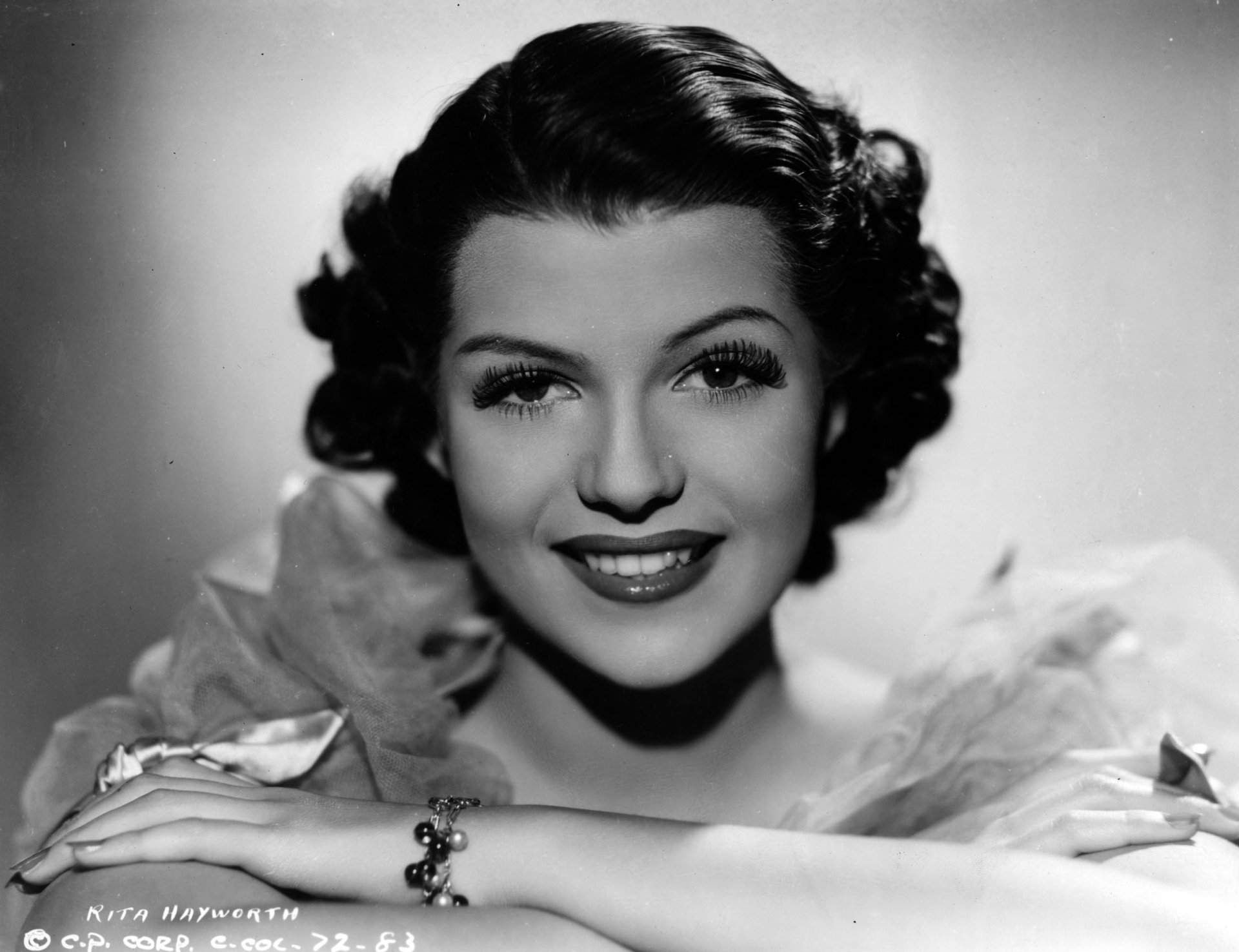 Black-and-white HD PC desktop wallpaper/background: close-up portrait of a smiling woman in classic Hollywood 1940s style, curled hair, ruffled collar and an elegant bracelet.