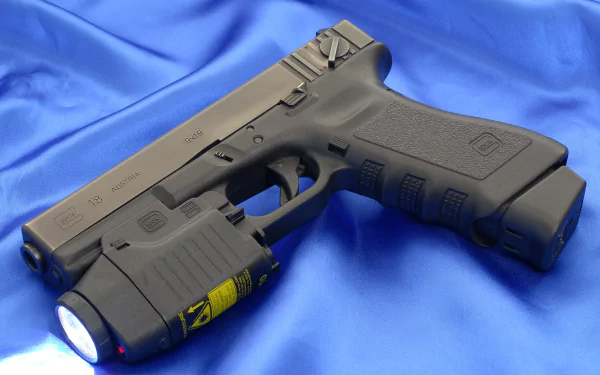 HD desktop wallpaper featuring a man-made Glock 18 pistol with an attached tactical flashlight on a blue fabric background.