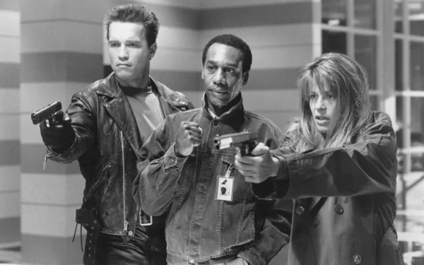 A black and white image from Terminator 2: Judgment Day featuring Arnold Schwarzenegger as the Terminator, Joe Morton as Miles Dyson, and Linda Hamilton as Sarah Connor, all wielding guns.