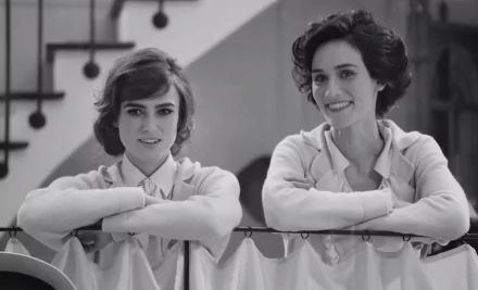 Black-and-white HD PC desktop wallpaper film still (2017): two young women in period clothing smiling and leaning on a railing inside a house.
