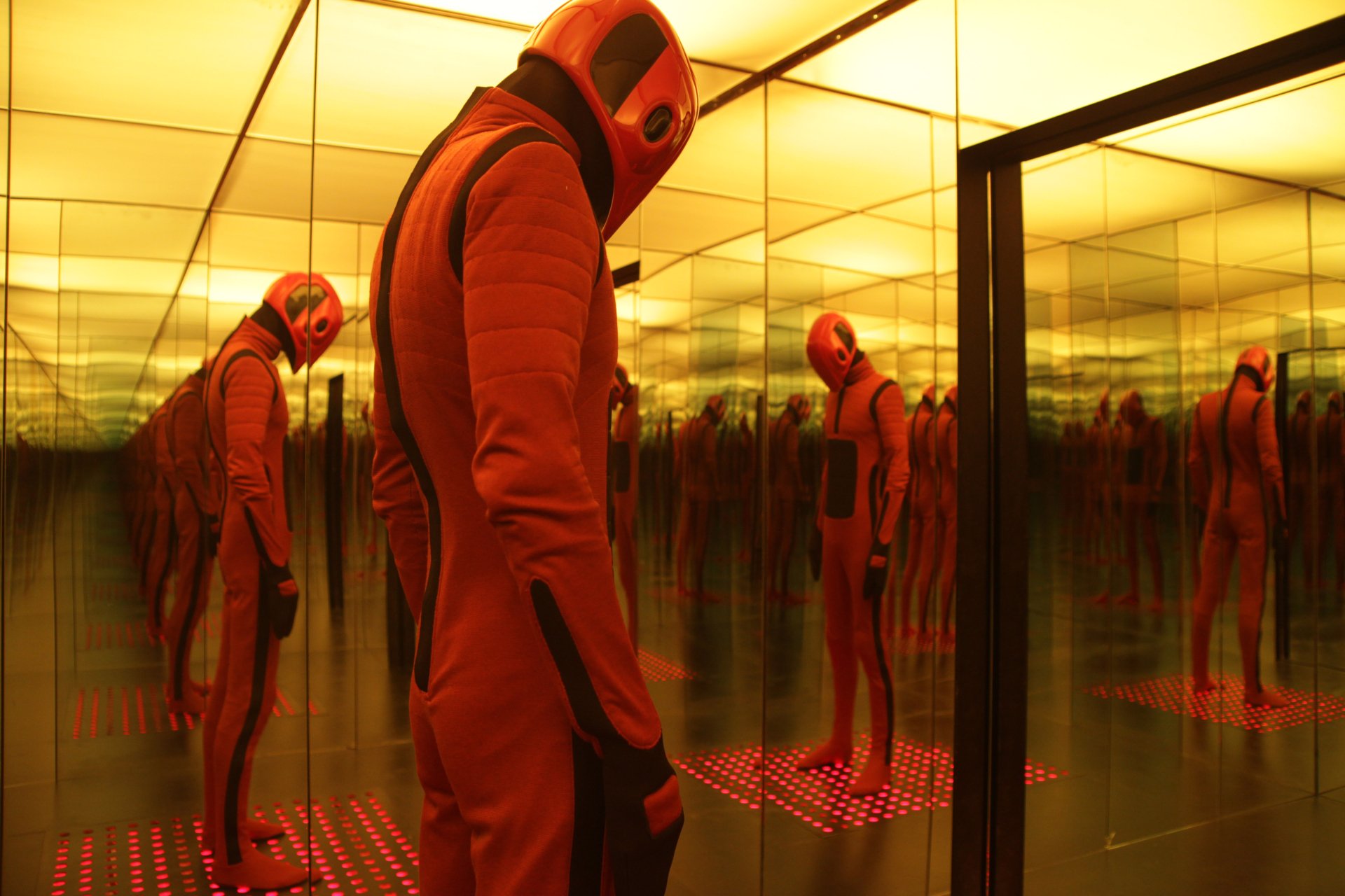 5K Ultra HD PC desktop wallpaper: still from the movie Beyond The Black Rainbow showing a red-suited figure in a mirrored, yellow-lit room with repeating reflections.