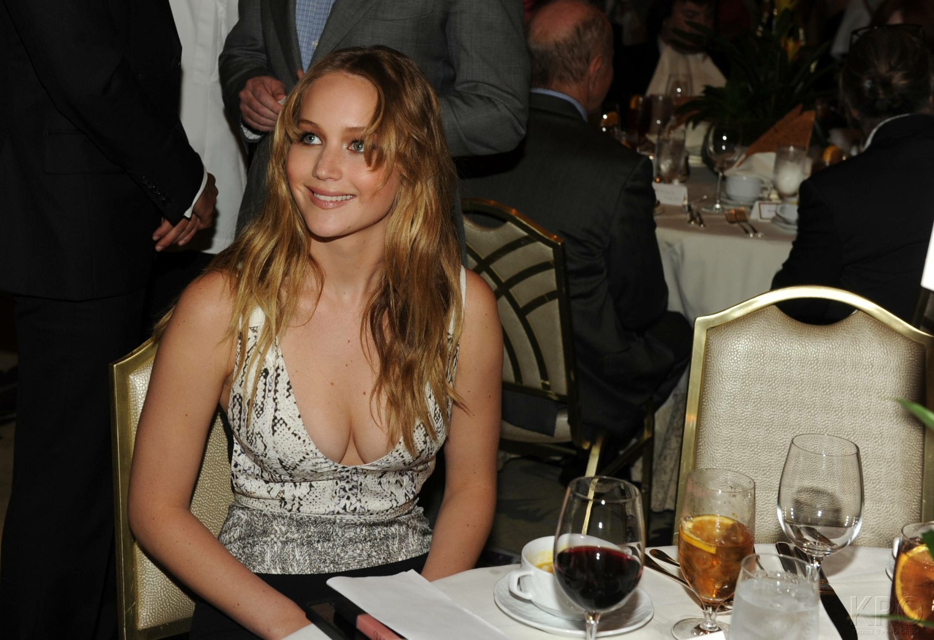 HD PC desktop wallpaper featuring celebrity Jennifer Lawrence smiling at a formal event, seated at a table with drinks and dinnerware.