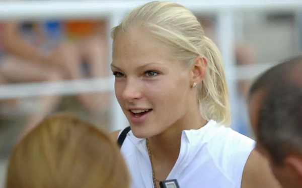 Smiling blond female athlete in a white jacket at a sporting event — HD PC desktop wallpaper background.