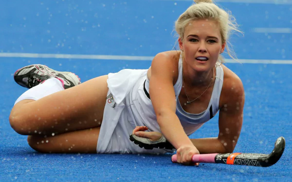 HD PC desktop wallpaper background: field hockey sports image — female player in white sliding on blue turf, reaching out with her stick in mid-play.
