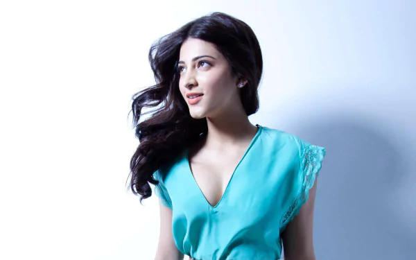 HD desktop wallpaper featuring celebrity Shruti Haasan, showcasing her in a teal outfit with flowing hair against a light background, exuding elegance and charm.