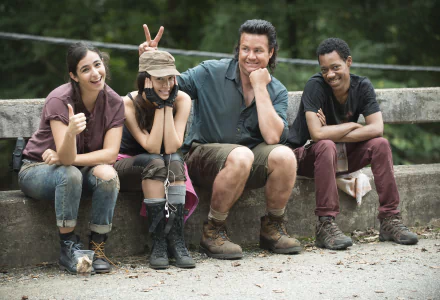 A lighthearted moment from The Walking Dead, featuring four characters sitting on a wooden railing, playfully posing for the camera with smiles and thumbs up. HD desktop wallpaper.