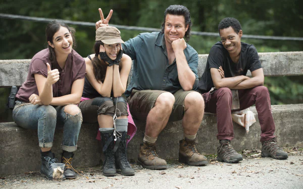A lighthearted moment from The Walking Dead, featuring four characters sitting on a wooden railing, playfully posing for the camera with smiles and thumbs up. HD desktop wallpaper.