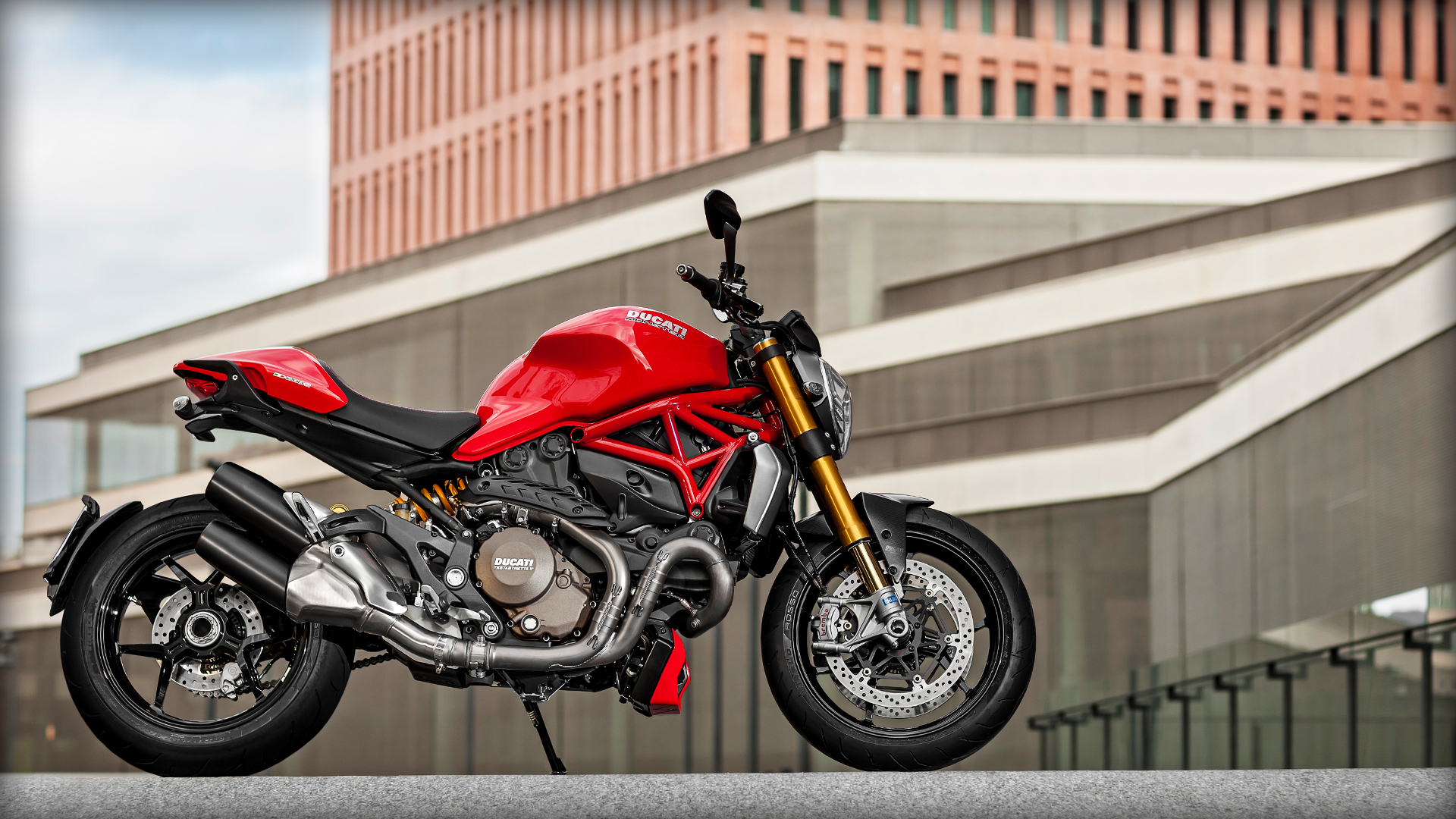 Vehicle: red Ducati motorcycle against modern urban architecture — HD PC desktop wallpaper background.