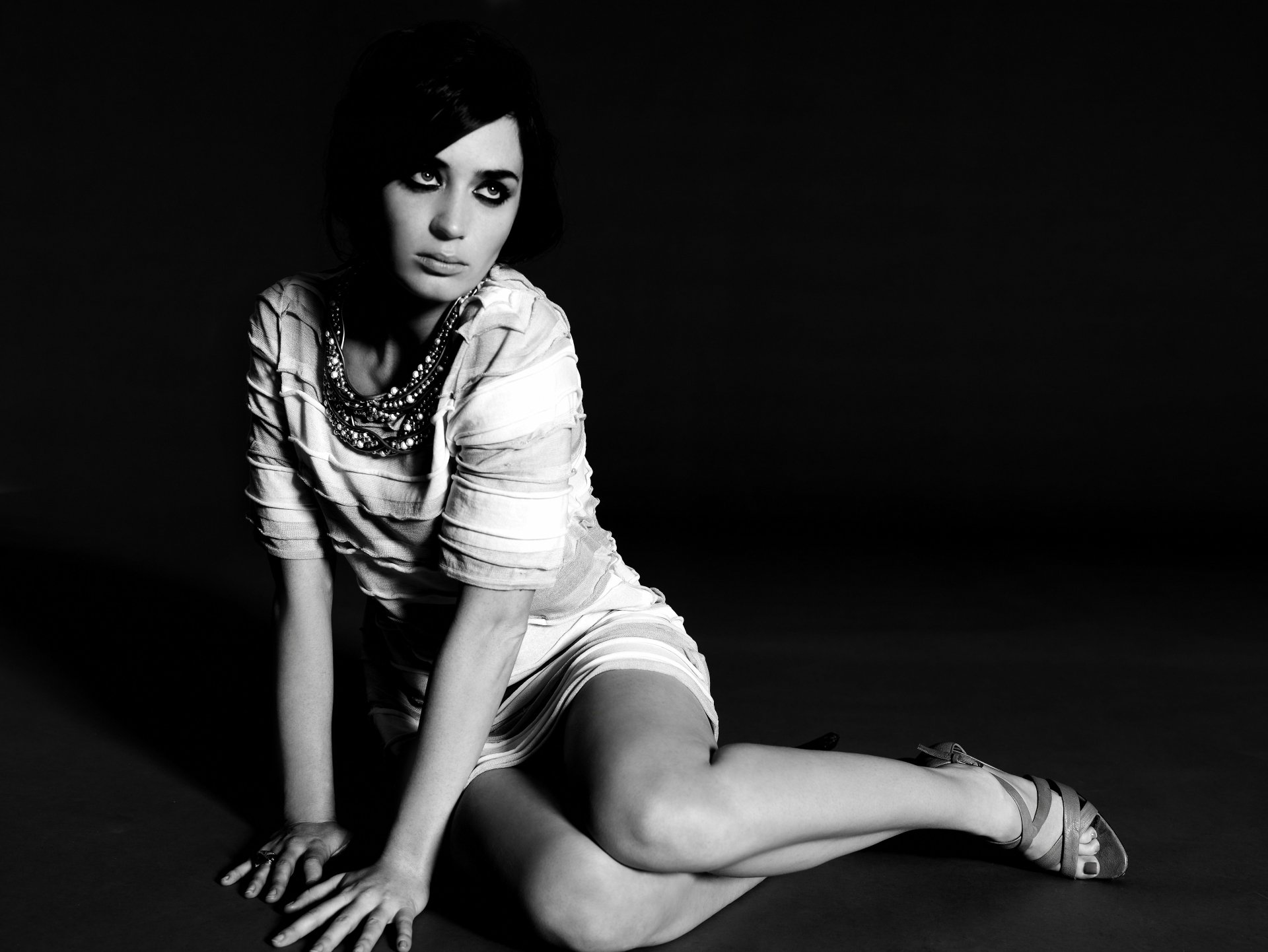 Black-and-white 5K Ultra HD PC wallpaper of a seated female celebrity in a short white dress and statement necklace against a dark background; identity unknown.