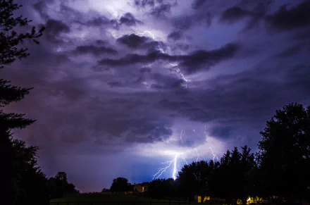 4K Ultra HD desktop wallpaper capturing a powerful lightning storm flashing through dark, dramatic clouds over a silhouetted treeline in nature.