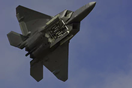 Lockheed Martin F-22 Raptor military jet with open weapons bay flying against a clear blue sky, featured as an HD PC desktop wallpaper background.