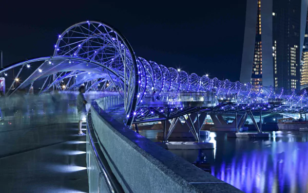 Night view of The Helix Bridge in Singapore, a man-made double-helix pedestrian bridge glowing blue over reflective water — 5K Ultra HD PC desktop wallpaper.