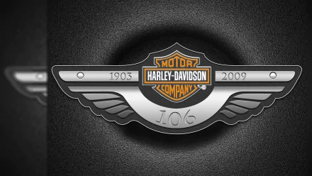 Harley-Davidson logo displayed on a sleek metallic emblem with wing details, set against a textured background in this HD PC desktop wallpaper.