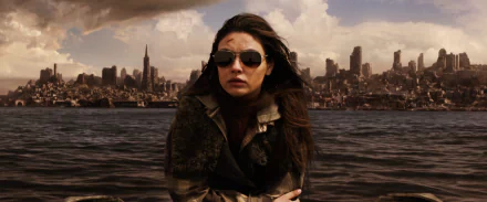 HD desktop wallpaper of Mila Kunis in a scene from the movie The Book of Eli, set against a dramatic cityscape backdrop.