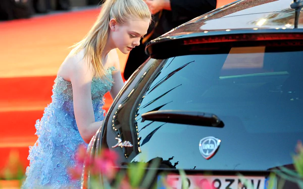 Young blonde woman in a blue tulle gown leaning into a black car on a red carpet, 2K Quad HD PC desktop wallpaper/background.