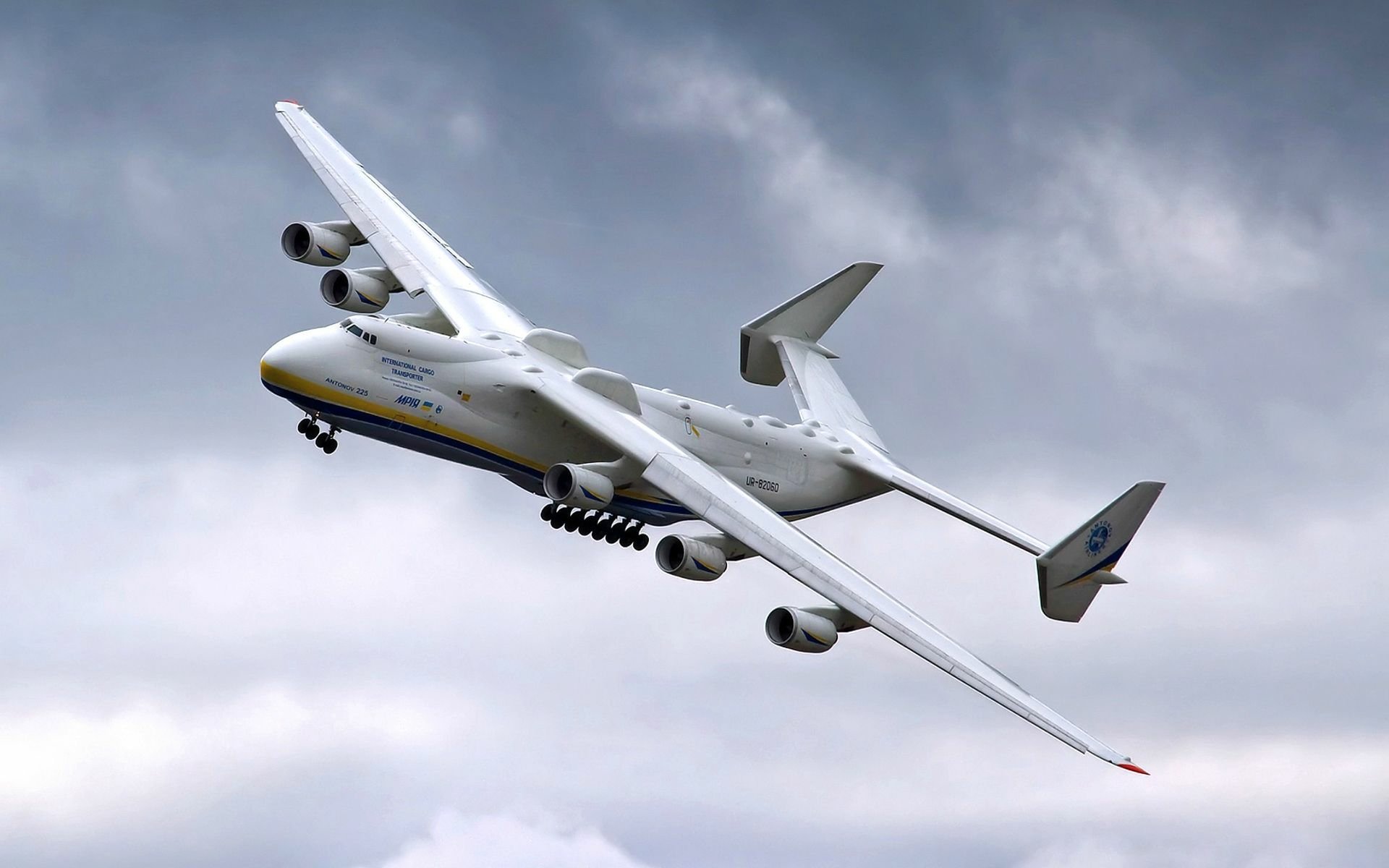 HD desktop wallpaper of the Antonov AN-225 Mriya, the largest cargo aircraft, soaring through a cloudy sky.