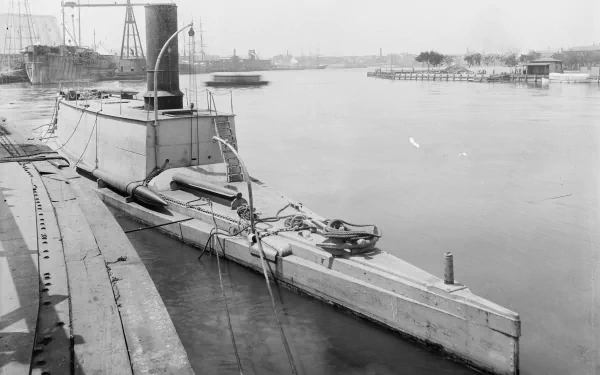Black-and-white 4K Ultra HD PC desktop wallpaper of a military torpedo boat moored in a calm harbor with industrial piers and distant ships.
