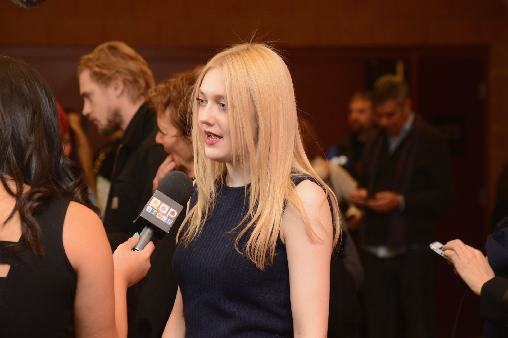 HD desktop wallpaper featuring celebrity Dakota Fanning engaged in an interview at a formal event, surrounded by people in the background.