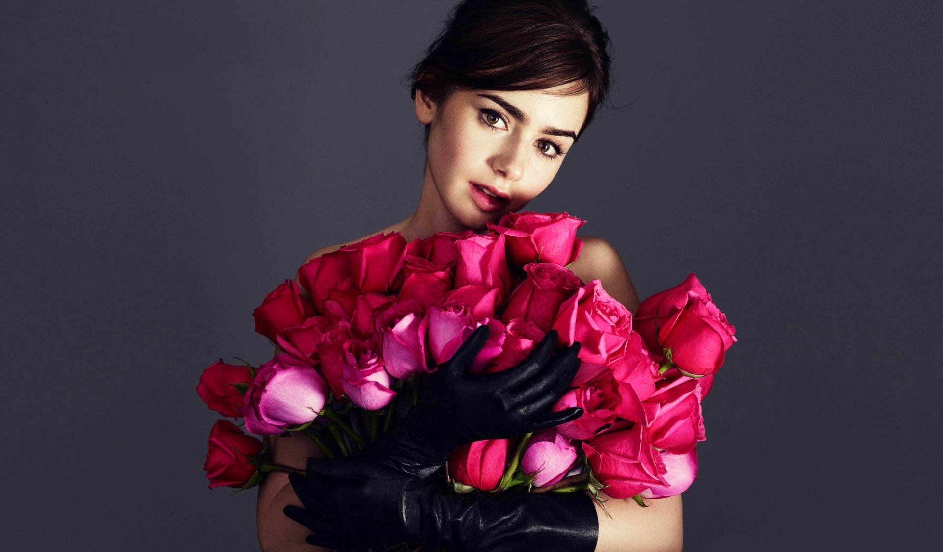 HD PC desktop wallpaper: celebrity portrait of a woman holding a bouquet of vibrant pink roses, wearing black gloves against a dark, minimalist backdrop.