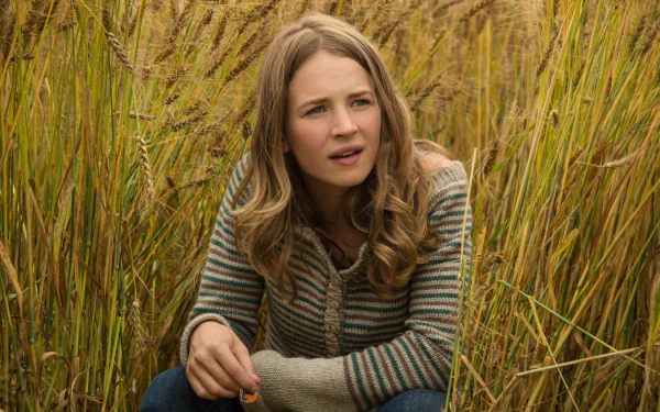 Brittany Robertson in a scene from the movie Tomorrowland, sitting among tall golden grass, looking contemplative. An HD wallpaper capturing a moment of reflection.