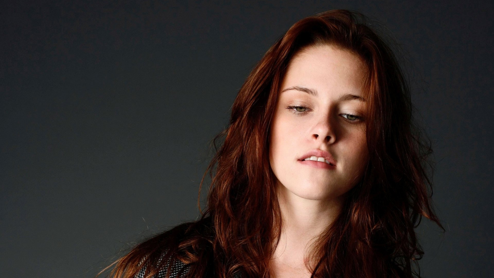 A striking HD desktop wallpaper featuring actress Kristen Stewart, showcasing her expressive gaze and wavy hair against a muted background.