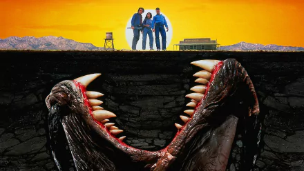 HD PC desktop wallpaper background for the movie Tremors: three people stand on a sunlit ridge while a massive toothy subterranean creature bursts from the dark earth below.