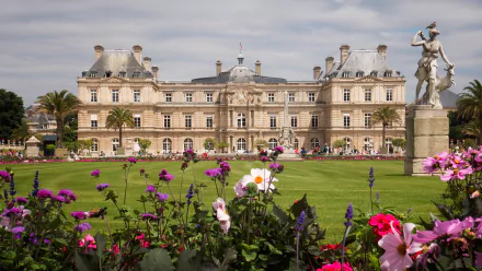 View of the Luxembourg Palace, home to the French Senate in Paris, with colorful flowers and a statue in the garden under a clear sky.