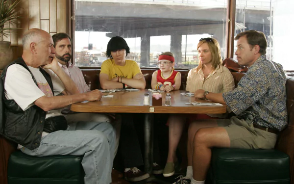 A scene from *Little Miss Sunshine* features characters played by Steve Carell, Toni Collette, Alan Arkin, Paul Dano, Greg Kinnear, and Abigail Breslin gathered around a table.