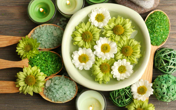 4K Ultra HD still life of spa elements featuring green and white flowers, lit candles, and green bath salts arranged on a wooden surface as a calming desktop wallpaper.