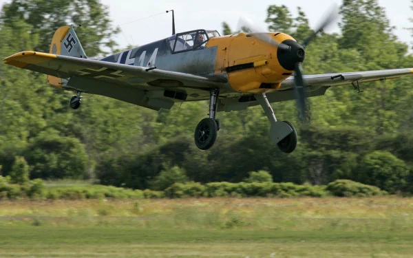 A Messerschmitt Bf 109 aircraft gracefully flies above a lush green landscape, showcasing its military design in this high-definition PC desktop wallpaper.
