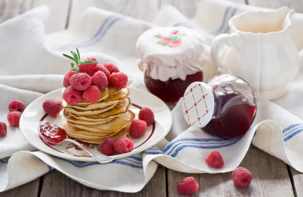 A stack of pancakes topped with fresh raspberries and raspberry jam, accompanied by jars of jam and a white creamer on a rustic wooden table, HD desktop wallpaper.