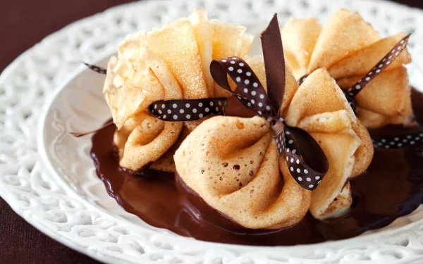 A beautifully arranged chocolate dessert featuring delicate crêpes tied with ribbons, served on an elegant plate, creating a tempting and luxurious HD wallpaper background.